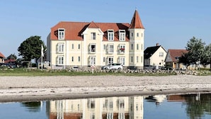 A large, multi-story building with a red roof, situated by a calm body of water reflecting its structure. - 4 Person Holiday Home in Hejls (Hejls)