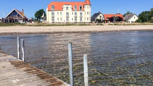 A waterfront hotel with a large building, a wooden dock, and a clear view of the water. - 4 Person Holiday Home in Hejls (Hejls)