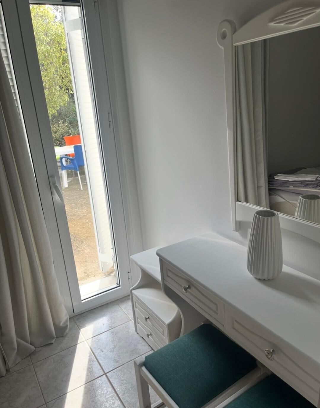 A room with a white vanity, a green bench, a mirror, and a door leading outside.