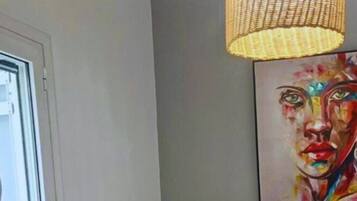 Una habitación con sofá, un cuadro, una ventana y una lámpara de fibra trenzada.