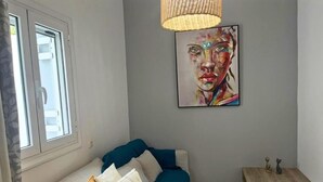 A room with a sofa, a painting on the wall, a window, and a small table with decorative items.