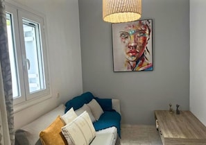 Et værelse med en sofa, et maleri på væggen, et vindue og et lille bord med pynt.