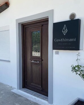Una puerta de madera oscura con un panel de vidrio, un cartel con el nombre 'Gosthimani Residence' y una planta pequeña al lado de la puerta.