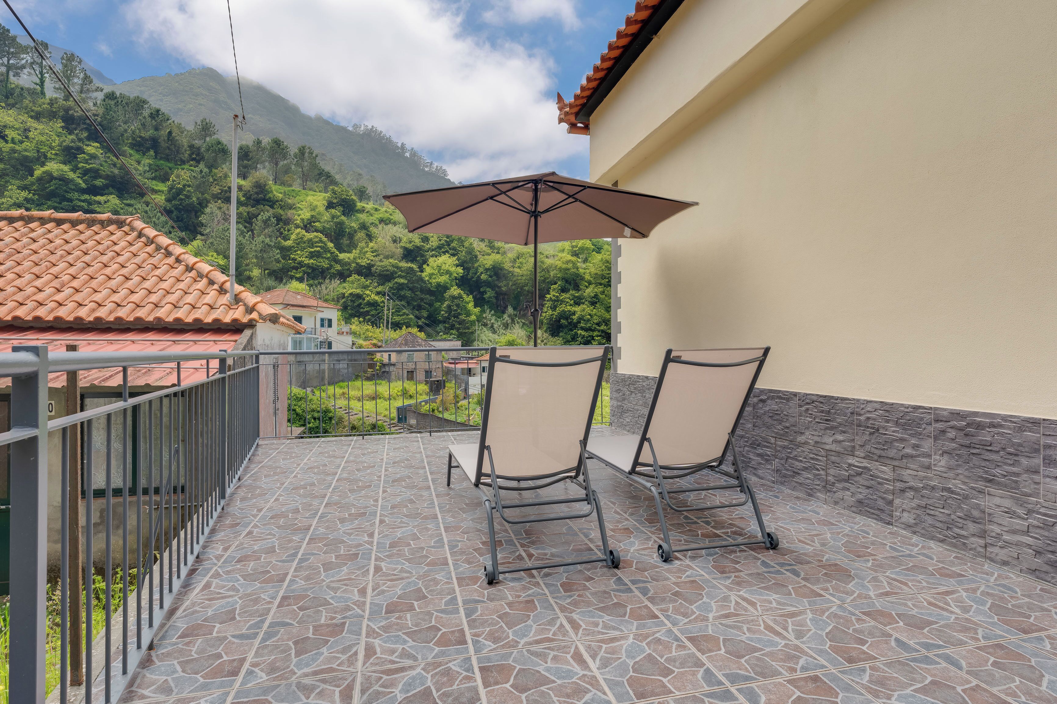 Ein Balkon mit zwei Stühlen und einem Sonnenschirm, mit Blick auf eine Berglandschaft.