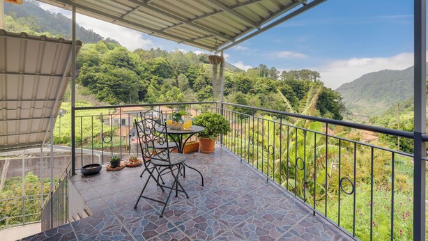 A balcony with a view of lush green hills, a table with chairs, and potted plants. - Gil House by Holiday Rental Madeira (São Vicente)