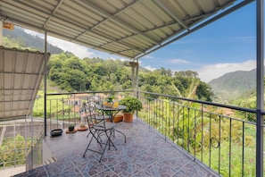Un balcon offrant une vue sur de douces collines verdoyantes, une table avec des chaises et des plantes en pot.