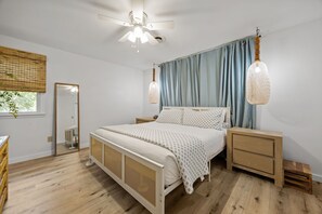 Ein Schlafzimmer mit einem Bett, Nachttischen, einem Deckenventilator und einem Fenster mit Vorhängen.