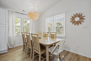 Ein Essbereich mit einem runden Tisch, sechs Stühlen, weißen Vorhängen und einer Wanddekoration im Sonnenstrahl-Design.