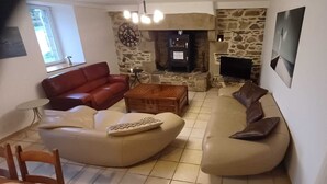 A living room with a stone fireplace, a red sofa, a beige sofa, and a coffee table. - Secret Refuge in Bretagne Mer & Nature à Deux Pas. (Tréduder)