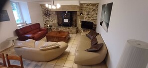 A living room with a stone fireplace, a red sofa, a beige sofa, and a coffee table. - Secret Refuge in Bretagne Mer & Nature à Deux Pas. (Tréduder)