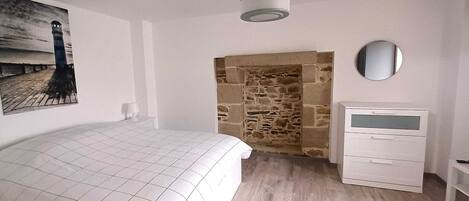 Een slaapkamer met een bed, een kaptafel, een spiegel en een stenen muur.