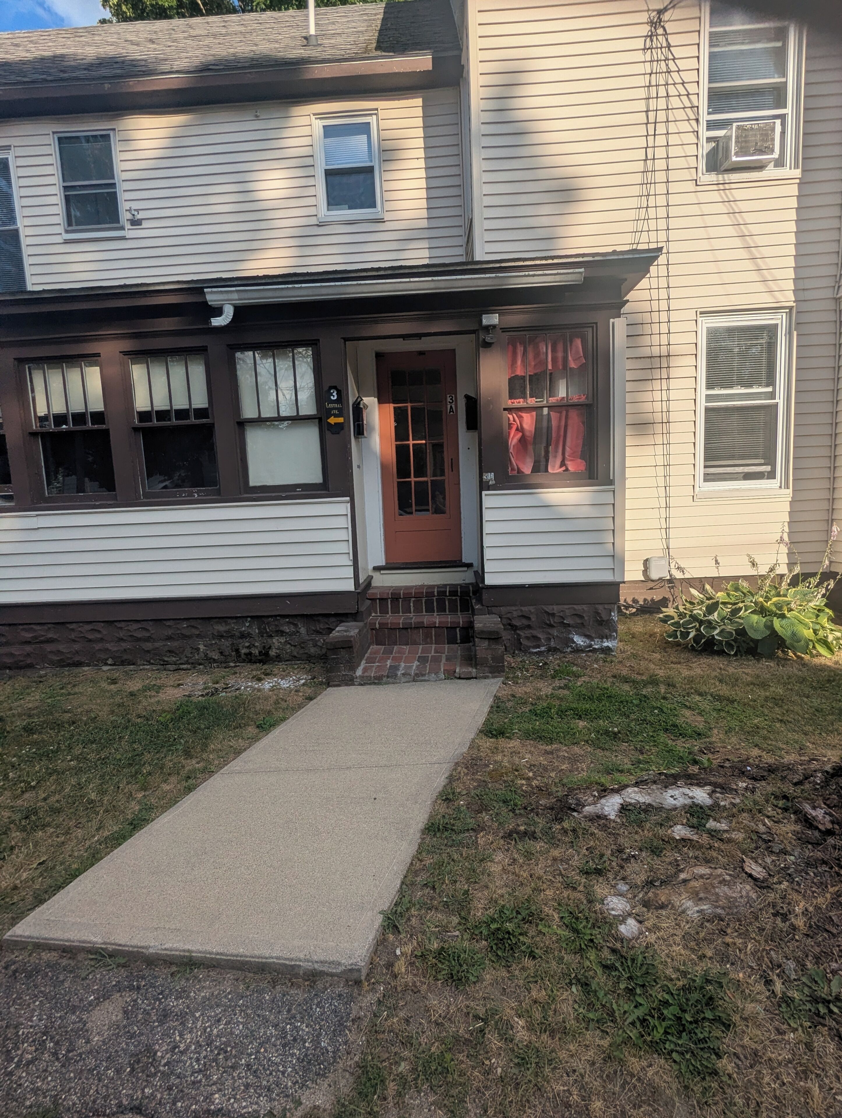A two-story house with a front porch, a red door, and a small brick step leading to the entrance.