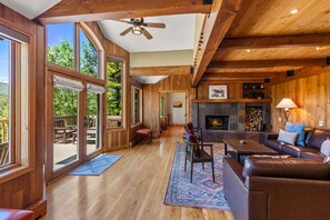 A spacious room with large windows, a fireplace, a ceiling fan, and a wooden floor. - Alpenview Lodge | Best Of Breck (Breckenridge)