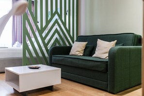 Ein modernes Wohnzimmer mit einem grünen Sofa, einem weißen Couchtisch und einer raumteilerartigen Wand mit geometrischem Muster.