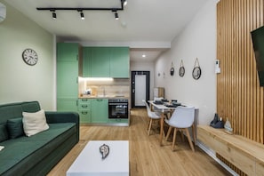 Eine moderne Wohnung mit einem grünen Sofa, einem Essbereich, einer Küche und einer Wand mit Holzverkleidung.