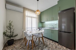A compact kitchen with a dining table, chairs, a refrigerator, and a potted plant. - Perla Apartment 2BR Beachside (Golem)