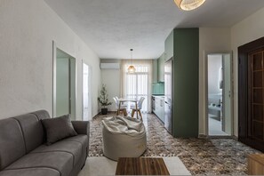 A modern living room with a sofa, a bean bag, a dining table, and a kitchen area. - Perla Apartment 2BR Beachside (Golem)