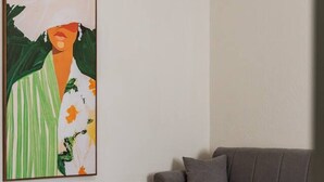 Ett vardagsrum med en grå soffa, ett träbord, en inramad abstrakt målning och en hängande lampa.