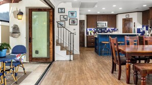 Una cocina moderna con armarios de madera, un comedor con mesa y sillas de madera, y una escalera que sube a un nivel superior.