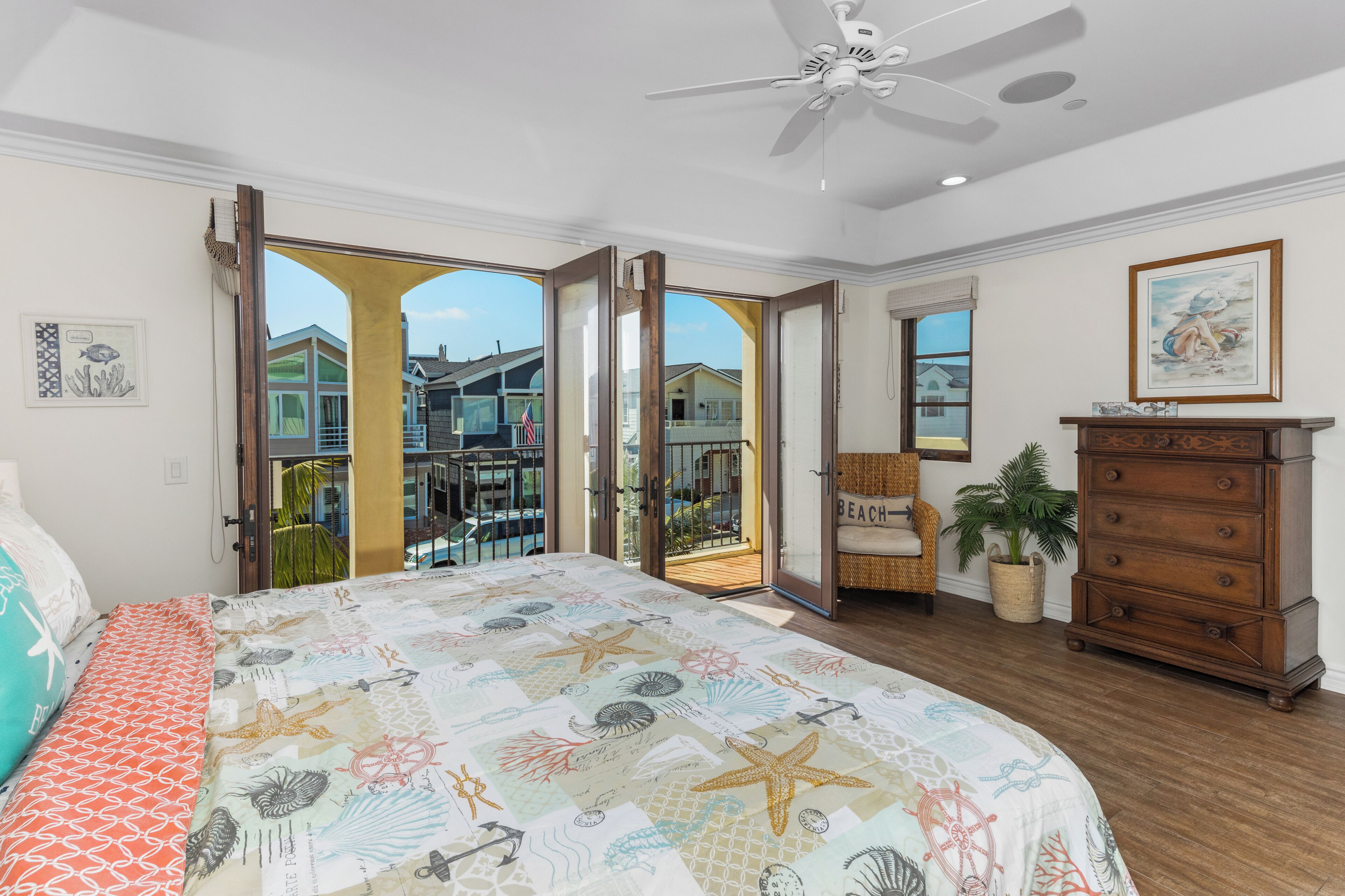 A bedroom with a large bed, a dresser, a ceiling fan, and a view of the outside.