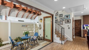 Un patio techado con muebles de mimbre, una escalera de madera y una zona de cocina con armarios de madera.