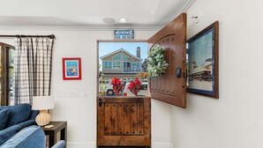 Una habitación con puerta de madera, sofá azul, una mesita con lámpara, un cuadro enmarcado y un letrero que indica camino único hacia la playa.