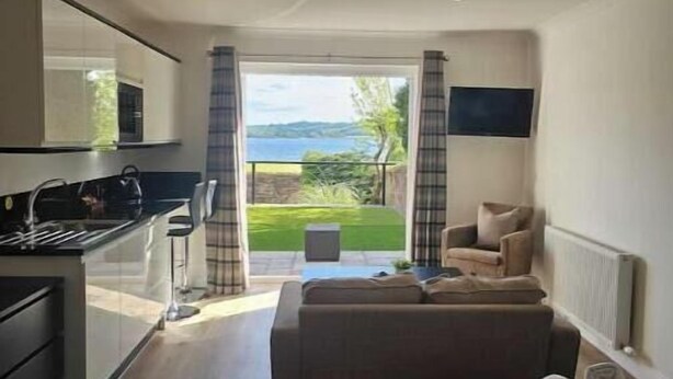 Una habitación de hotel moderna con kitchenette, sofá, cama y vistas al exterior.