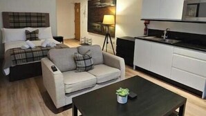 Un espacio habitable compacto con una cama, dos sofás, una mesa de centro, una zona de cocina y un cuadro en la pared.