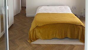 A bedroom with a bed, a white ceiling, a wooden floor, and a hallway leading to another room. - Petite Eze (Provence-Alpes-Côte d'Azur)