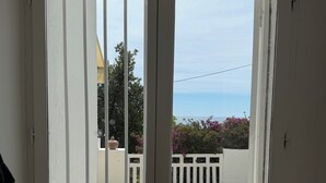 A view through a door with white vertical bars, leading to a balcony with a white railing, a gravel path, and a clear sky. - Petite Eze (Provence-Alpes-Côte d'Azur)