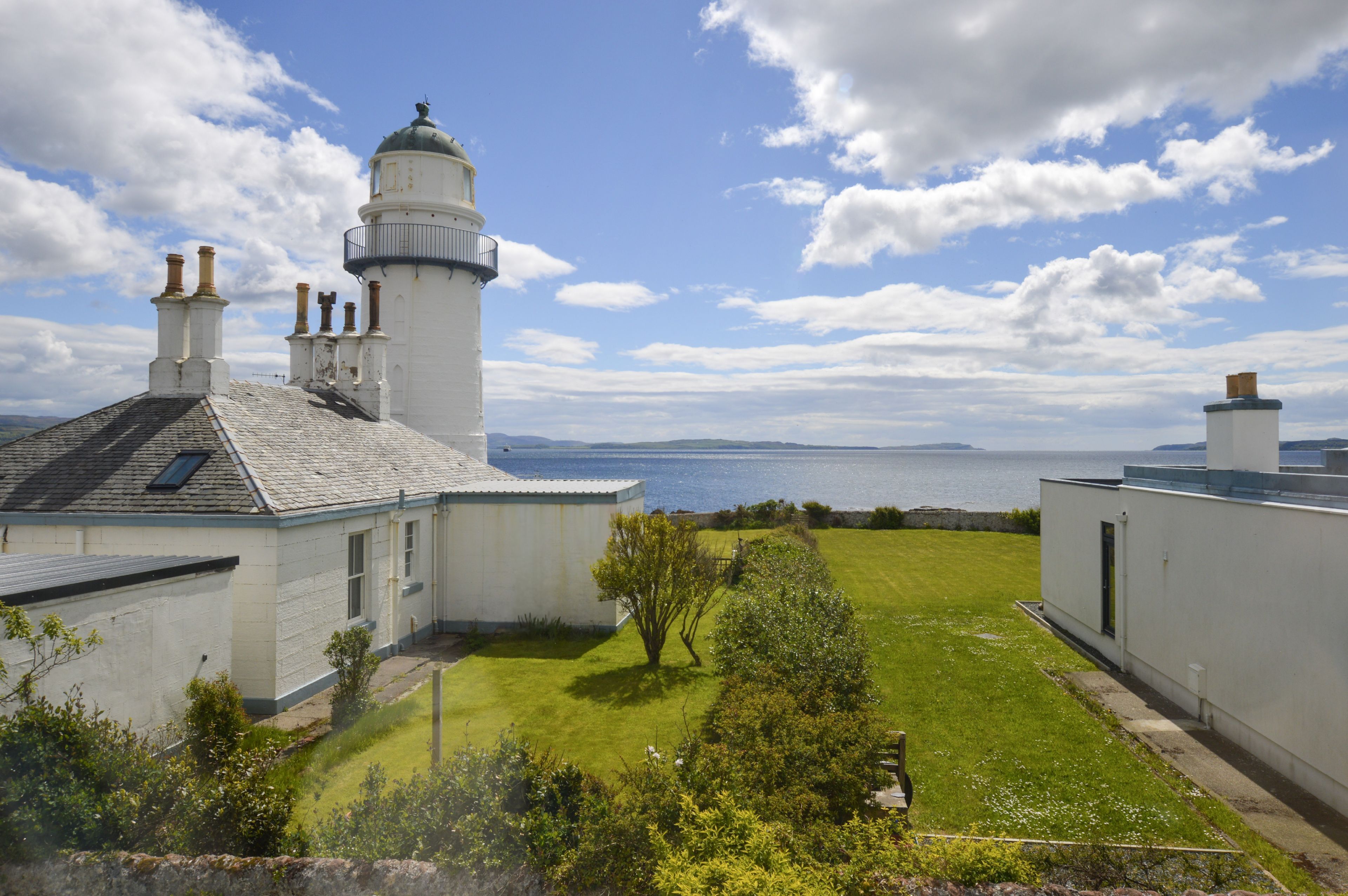 A lighthouse with a white exterior, a grassy yard, and a view of the sea.