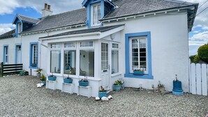 Une maison blanche aux bordures bleues, avec un porche et des plantes en pot.