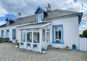 Un bĂątiment blanc avec des bordures bleues, un porche couvert et des plantes en pot.