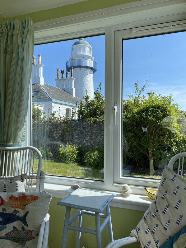 Une chambre avec vue sur un phare, une petite table et une chaise dotĂ©e dâun coussin Ă motifs de poissons.