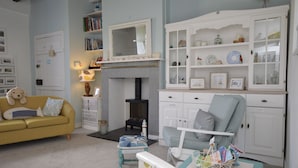 Un salon chaleureux avec un canapé jaune, un fauteuil bleu, une cheminée et un meuble blanc aux portes vitrées.