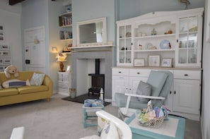 Un salon comprenant un canapé, un fauteuil, une cheminée, une bibliothÚque et une table à manger avec un panier de magazines.