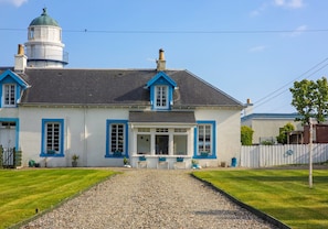 A two-story house with a white exterior and blue trim, a gravel driveway, and a white picket fence.