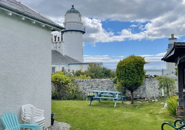 A lighthouse, a stone wall, a picnic table, and a grassy area.