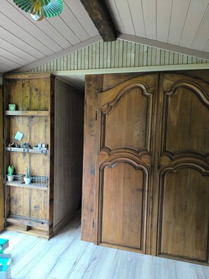 A wooden wardrobe with a mirror, a shelf with decorative items, and a wooden floor.