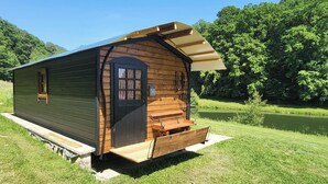 A small wooden cabin with a door, windows, and a bench outside. - "La Maison Nomade" vacation rental in a paradise-like setting. Woods. Ponds. Very quiet (CHAGNY)
