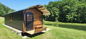 Une petite cabane en bois avec une porte, des fenêtres et un banc à l’extérieur.