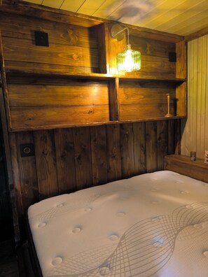 Une tĂȘte de lit en bois avec un Ă©clairage intĂ©grĂ©, un matelas blanc recouvert dâun tissu texturĂ© et une table de chevet en bois sur laquelle repose un petit objet.