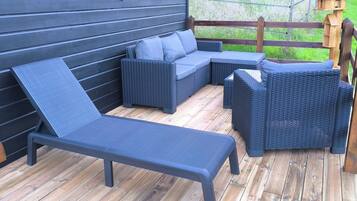 Eine Terrasse mit einer dunkelgrauen Couch, einem Liegestuhl und einem Holzzaun.