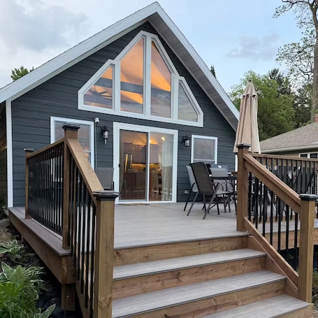 A modern house with a steep gable roof, a deck with outdoor furniture, and a staircase leading to the entrance.. Edgewater Escape