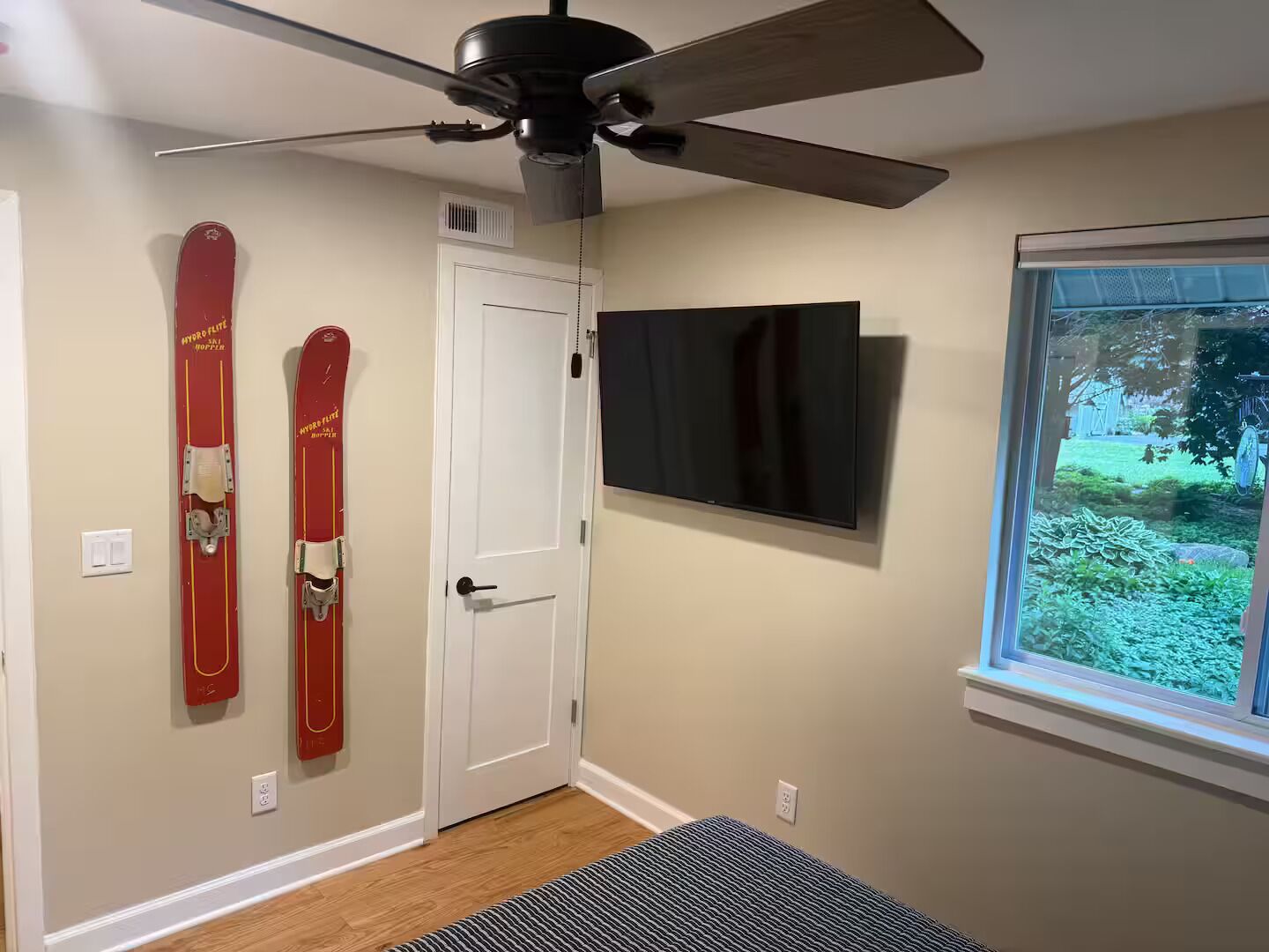 A room with a ceiling fan, a mounted TV, and skis on the wall.