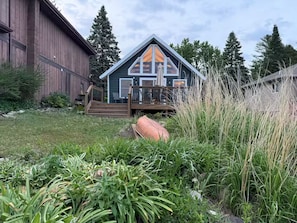 A house with a large deck, a garage, and a yard with various plants.