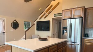 Una cocina con una isla grande, armarios de madera, un refrigerador de acero inoxidable y un televisor de pantalla plana montado en la pared.