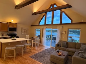 A spacious living area with a kitchen, dining area, and a large sliding glass door leading to a balcony with a lake view.