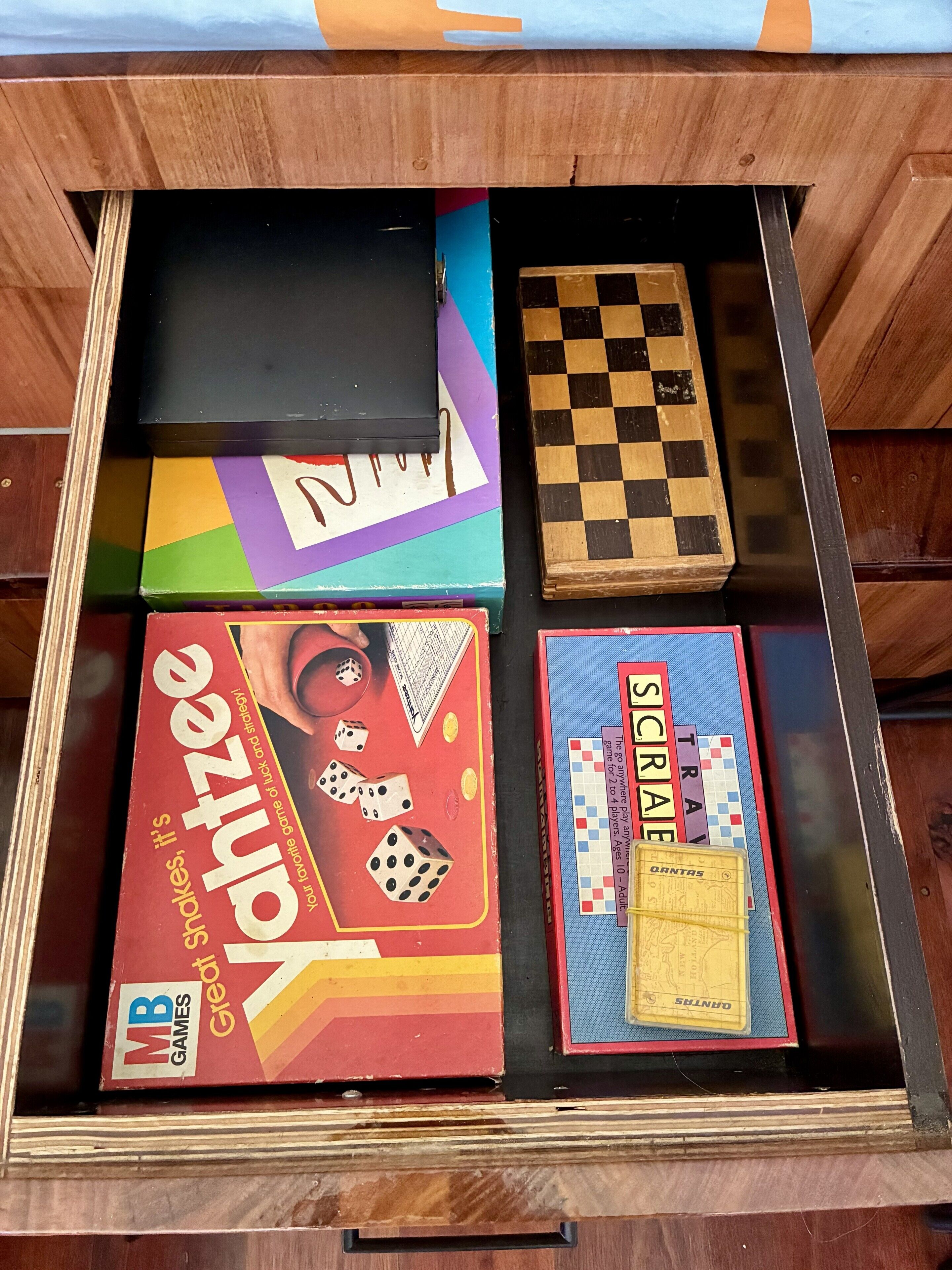 Uma gaveta de madeira com vários jogos de tabuleiro, incluindo cobra e escada, damas e Scrabble.