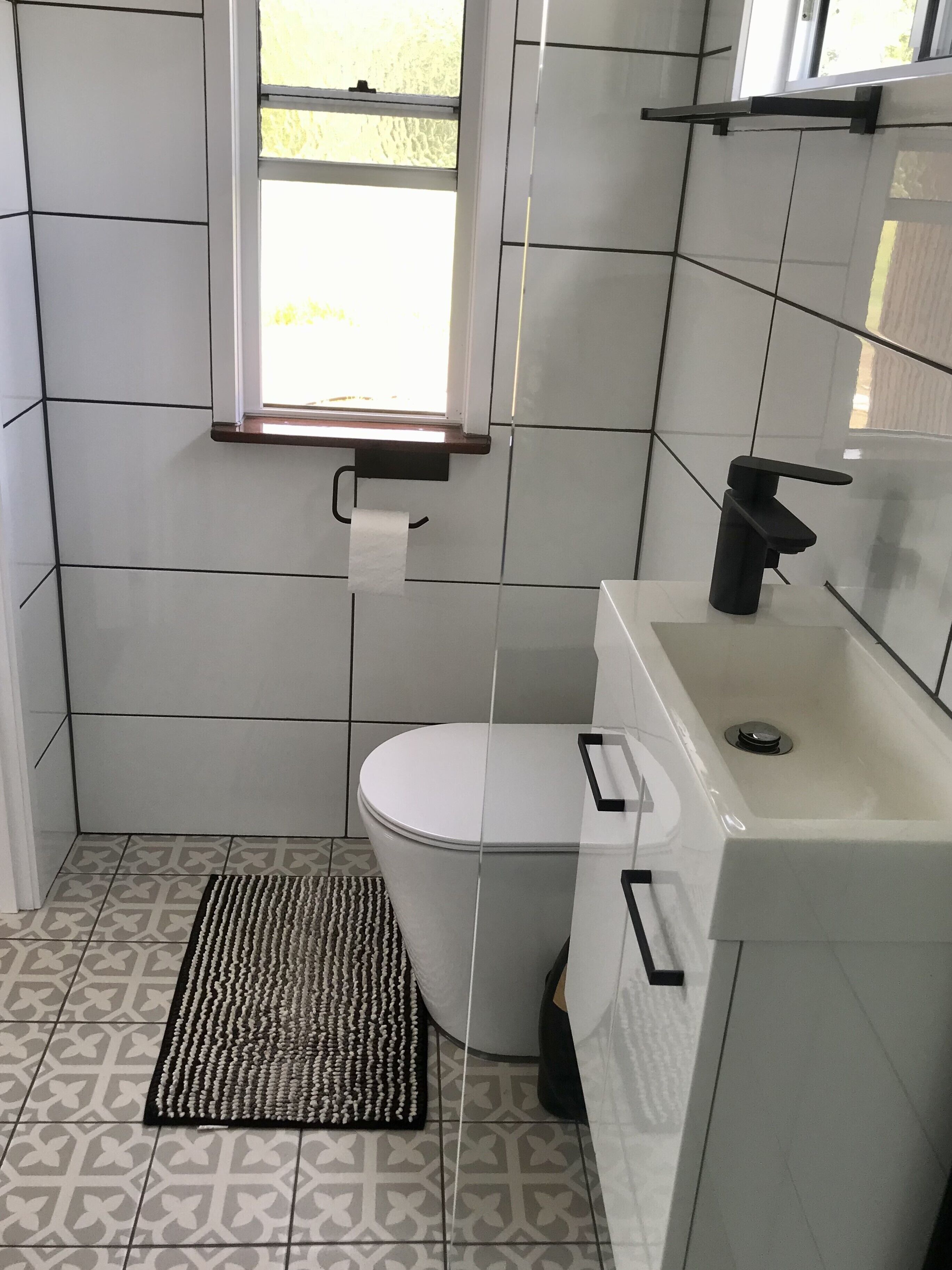 Une salle de bain avec des toilettes, un lavabo, une fenêtre et un carrelage décoratif.